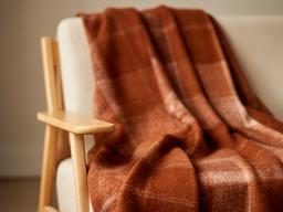 Roestkleurige wollen plaid over een houten fauteuil